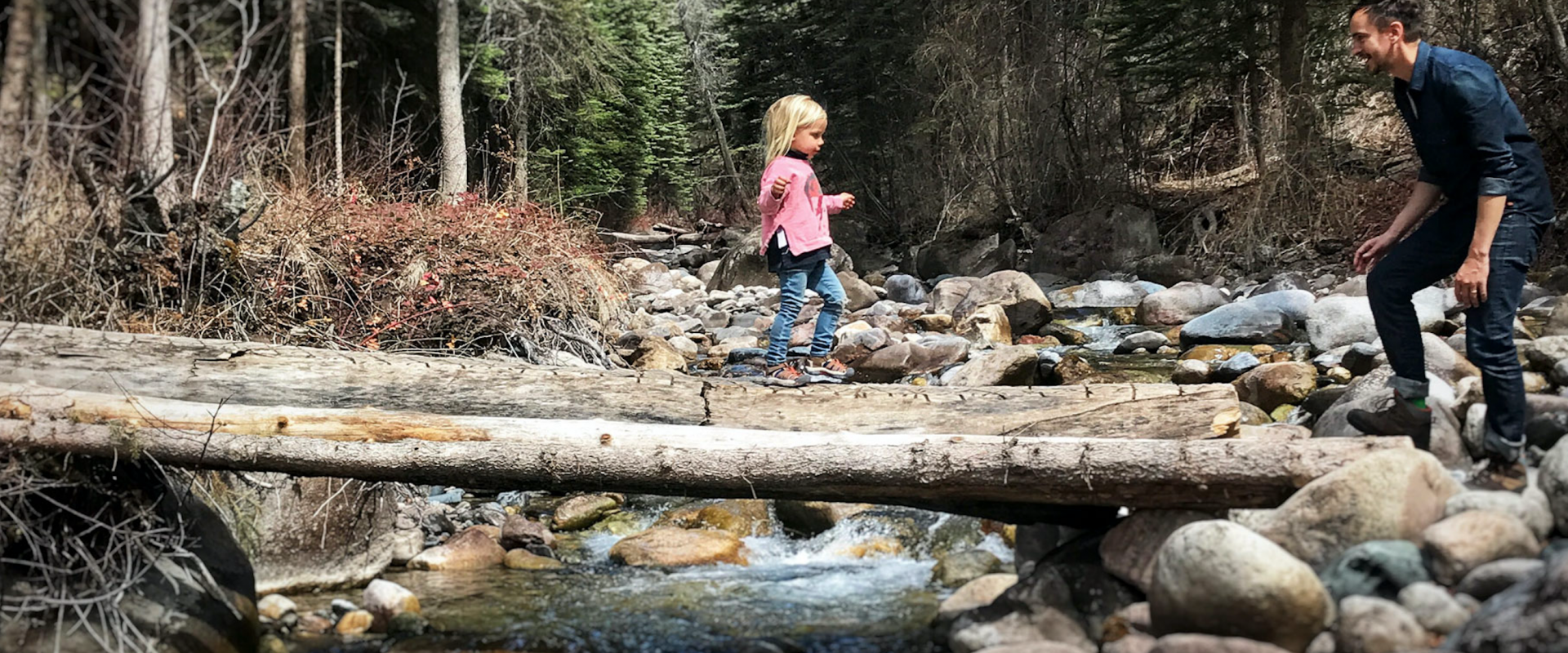 Détente et loisirs : petite fille avec un pull rose qui traverse un pont de bois pour rejoindre son papa. arrière-plan forêt avec rivière et rocher